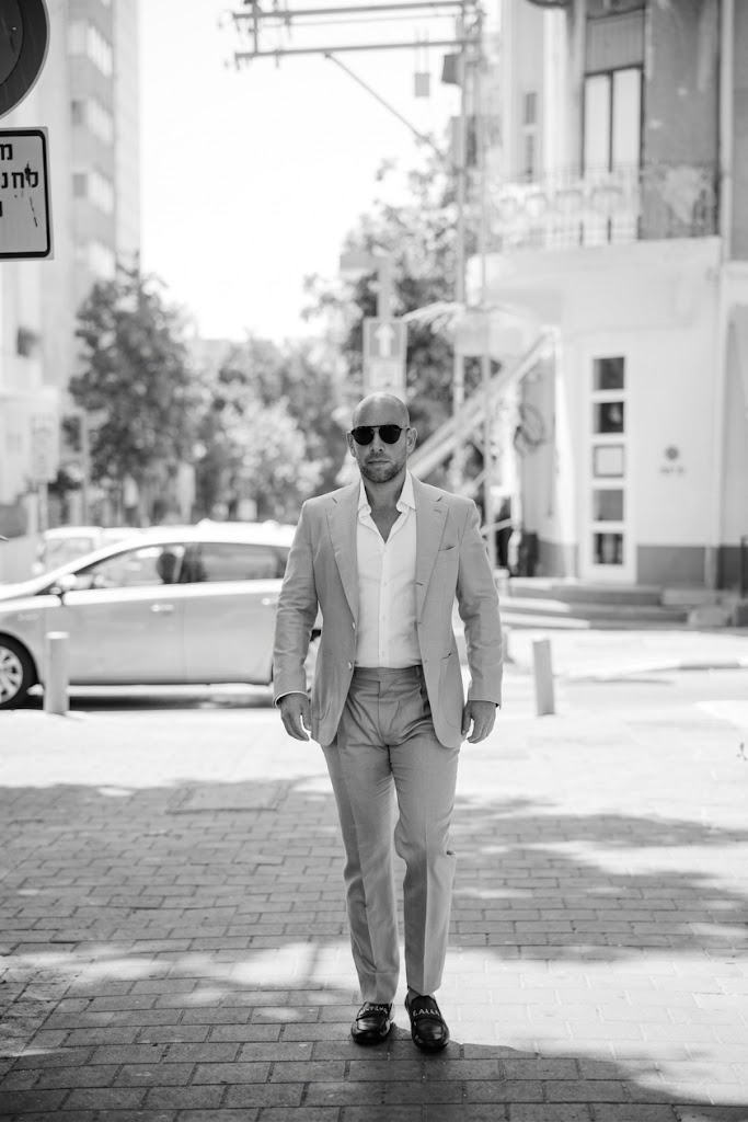 Aviv Leshem walking through a Tel Aviv street in a light suit